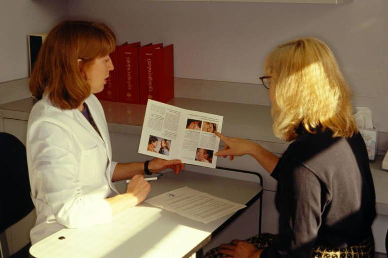 A woman is holding up a magazine while talking to another person.